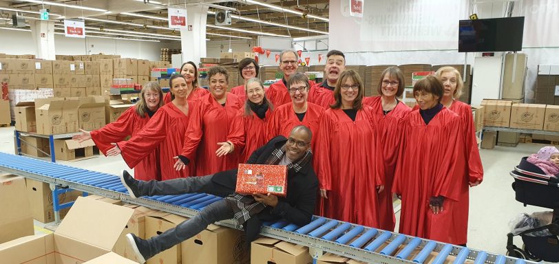 Der ONE VOICE GOSPEL CHOIR BERLIN in einer der Hallen von Weihnachten im Schuhkarton, mit Kirk Smith, der auf einem der Förderbänder liegt