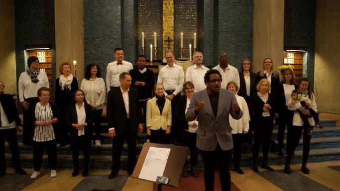 Foto des ONE VOICE GOSPEL CHOIR BERLIN während des Gottesdienstes: der Chor steht auf den Stufen vor dem Altar und singt.