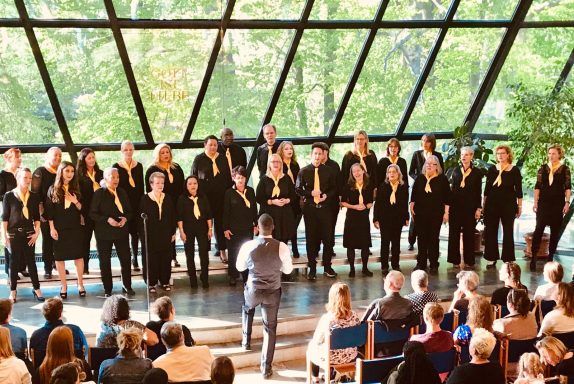 Der ONE VOICE GOSPEL CHOIR BERLIN vor der riesigen Glasfront des St. Michaelisheims in Berlin. 