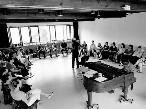 Die Mitglieder des neu gegründeten ONE VOICE GOSPEL CHOIR BERLIN sitzen im Halbrund erwartungsvoll um ihren Chorleiter Kirk Smith herum