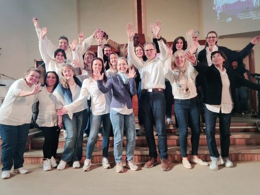 Der ONE VOICE GOSPEL CHOIR BERLIN in der Kiezkirche Rixdorf: alle sind in blau und weiß gekleidet, halten die Arme in die Luft und winken