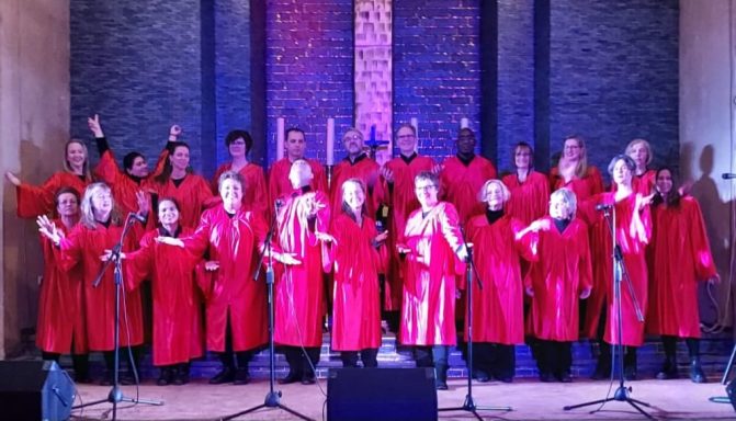 Der ONE VOICE GOSPEL CHOIR BERLIN steht vor dem Altar der GAK. Alle haben ihre roten Roben an und präsentieren sich glücklich.