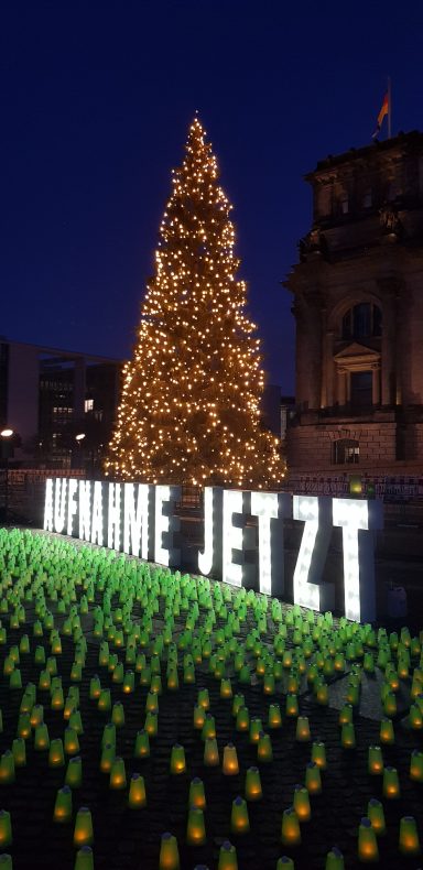 Vor einem erleuchteten Weihnachtsbaum steht in großer Leuchtschrift Aufnahme Jetzt