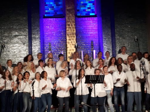 Die Workshop-Teilnehmer des ONE VOICE GOSPEL CHOIR BERLIN singen in der bunt erleuchteten Gustav-Adolf-Kirche Berlin